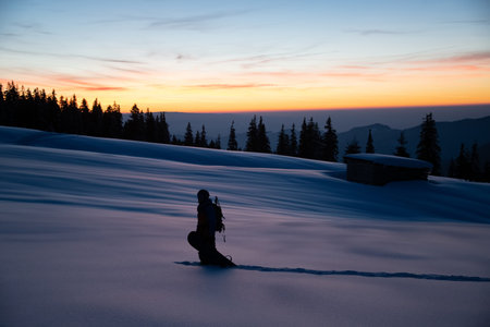 beautiful view of man with snowboard on deep powdery snow against the backdrop of sunset sky and treesの写真素材