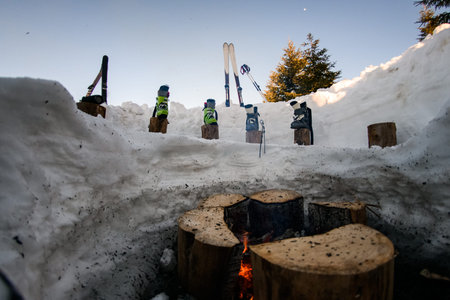ski equipment and ski boots are in a row on wooden stumps near the fire