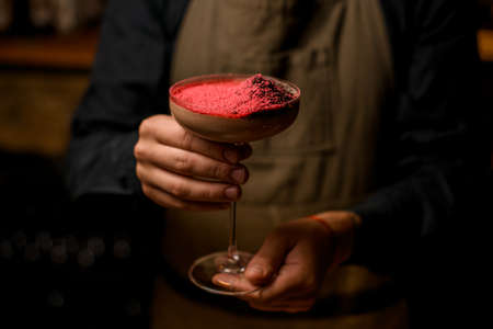 Male bartender in brown apron holding in hands brown alcohol cocktailの写真素材