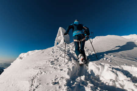 rear view of a man in a bright ski suit with ski poles climbing up a snow trailの写真素材