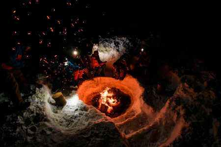 high angle view of campfire with flying sparks and group of tourists sitting and basking around it
