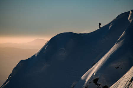 Amazing view of a snow-covered hill with powdery snow and a man skier on it. Picturesque landscape and the sky in the background. Ski touring and freeride conceptの写真素材