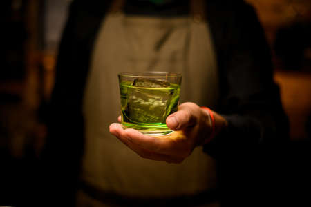 front view of glass with a green drink on the hand of a male bartenderの写真素材