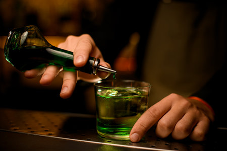 Selective focus of bottle with green essences, a drop of which adds to glass with a cocktailの写真素材