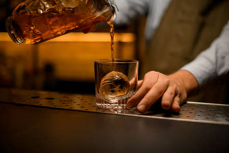 view of glass with piece of ice into which beverage is pouredの写真素材