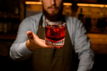 great front view of glass with bright drink which hand of a male bartender gently holdsの写真素材