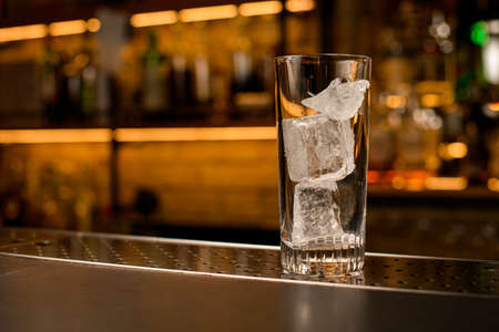 front view of transparent cocktail glass with ice cubes on bar counterの写真素材