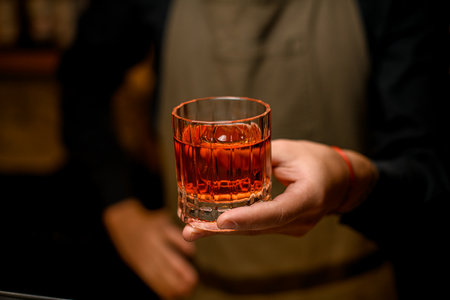 hand of bartender hold old-fashioned glass with alcoholic drink and a piece of iceの写真素材