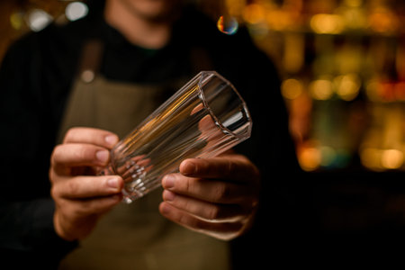 selective focus of empty tall glass for drink in hands of male bartender
