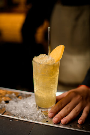 close-up of cocktail glass with ice garnished with pineapple slice and steel drinking straw.