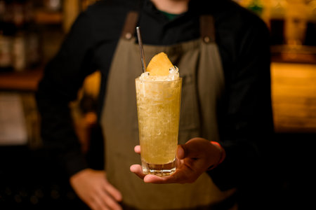 selective focus of cocktail glass with ice garnished with pineapple slice and steel drinking straw on male handの写真素材