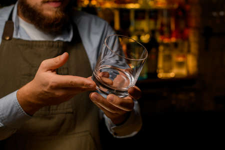 view of the hands of a male bartender holding a transparent empty glass for boozeの写真素材