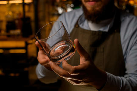 Close-up of clean empty glass for drinks in hands of male bartender.の写真素材