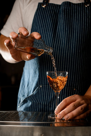 hand of bartender holds bottle with an alcoholic drink and pours into a wine glassの写真素材