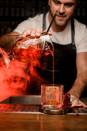 bartender holds mixing cup with red cocktail and pours it into a glassの写真素材