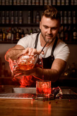 bartender holds mixing cup with a cocktail and pours a drink into a glassの写真素材