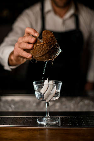 piece of coconut in a male hand over cocktail glass with drinkの写真素材