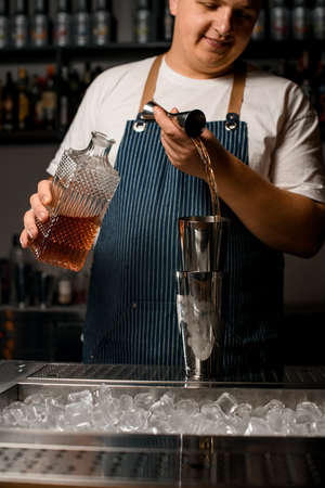 male bartender pouring alcoholic drink from steel jigger into shaker cupの写真素材
