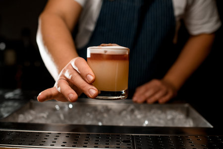 Close-up of male hand holding glass with foamy alcoholic cocktail over bar surface