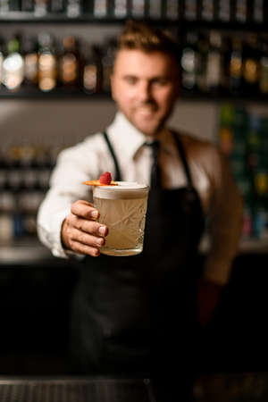 selective focus on glass with foamy cocktail decorated with orange slice and a raspberry in male handの写真素材