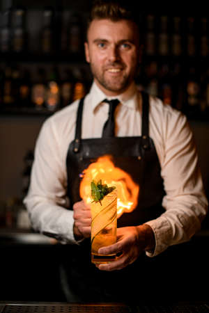 bartender holds glass of cocktail with cucumber slices and mint and sprinkles and sets it on fireの写真素材