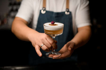 Hand of male bartender gently holds transparent glass with foamy alcoholic cocktailの写真素材