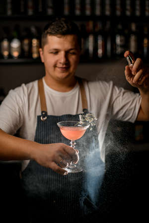 Bartender holds glass with pink alcoholic cocktail decorated with flover twigの写真素材