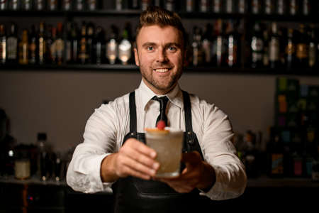 bartender serving a glass with fresh foamy and decorated cocktail to youの写真素材