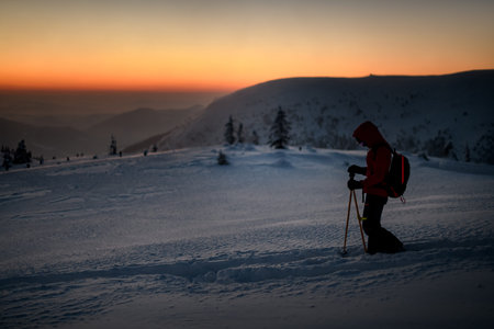 side view of skier with hiking equipment walking at deep snow on mountain slope.