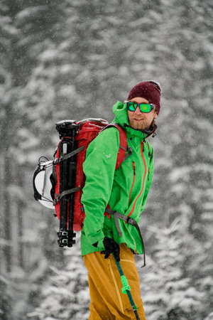 Side view of smiling male skier in goggles and and windproof clothes with ski poles in his hand
