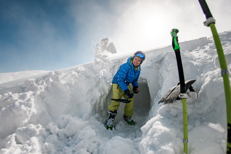 man in jacket with goggles and ski helmet holds shovel and scatters snow