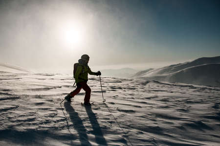 man in green and red ski suit with trekking poles walks through deep powdery snowの写真素材