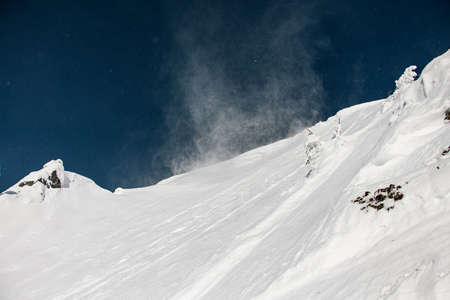 Snow covered mountain peaks sunlit and blown by the windの写真素材