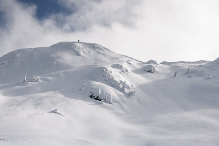 view of snow-capped mountain against the backdrop of the sky with man on top