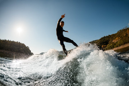 active sports man in wetsuit balancing on splashing wave on a wakesurf