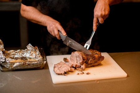 man chef cuts cooked fried meat on white cutting board.