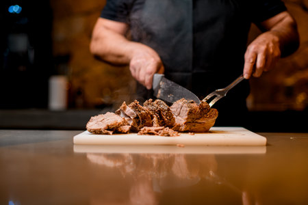Selective focus on delicious fried meat which man cuts to slices on cutting board.の写真素材