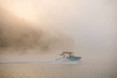 wonderful view on boat quickly floating on the water against the backdrop of silhouette of hill in fogの写真素材