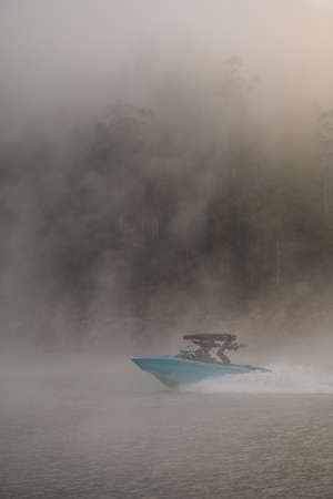 amazing view on boat quickly floating on the water against the backdrop of silhouette of hill in fogの写真素材