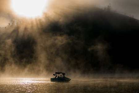 great scenic view of motorboat sailing on bay water among the hills covered with fogの写真素材