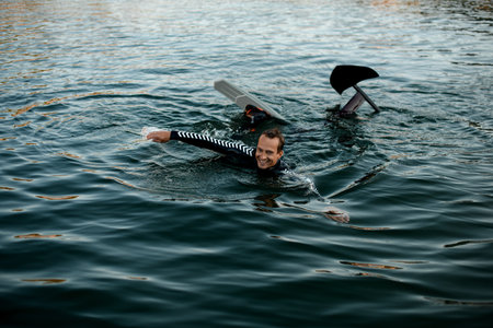 smiling man in wetsuit with a foil wakeboard swims in the waterの写真素材