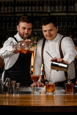 two bartenders preparing cocktails and pouring beverages into glasses on bar counterの写真素材