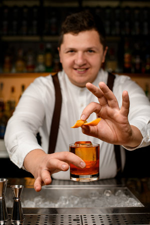 selective focus male hand holding glass with alcoholic drink and garnishing it with orange zest