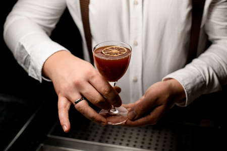Close-up of hands of bartender serving alcoholic cocktail in wineglassの写真素材