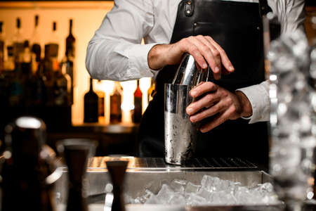 selective focus on shiny steel shaker on the bar counte, which is held by the hands of a male bartenderの写真素材