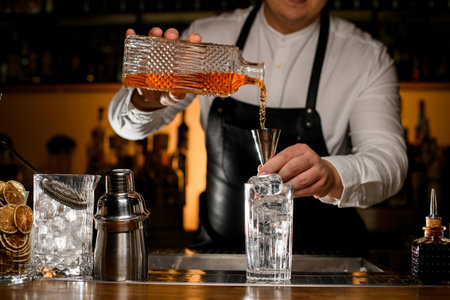 Close-up view of male bartender hand holding crystal bottle and pours beverage into steel jiggerの写真素材