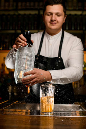 man bartender holds a siphon and splashes on glass with a cold cocktailの写真素材