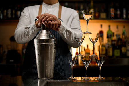 Close-up view of large shaker and pyramid of empty glasses stands on barの写真素材