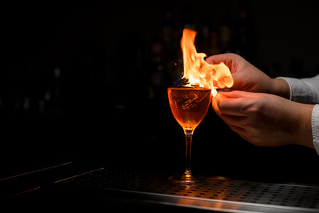 beautiful view on wineglass with cold drink and hands of bartender splash and set it on fireの写真素材