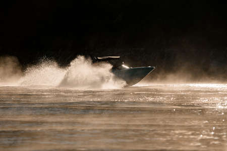 gorgeous side view of motorboat moving fast on the water and splashing drops from the wave around itの写真素材